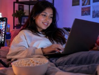 Mujer usando un portátil junto a un smartphone con una red social abierta